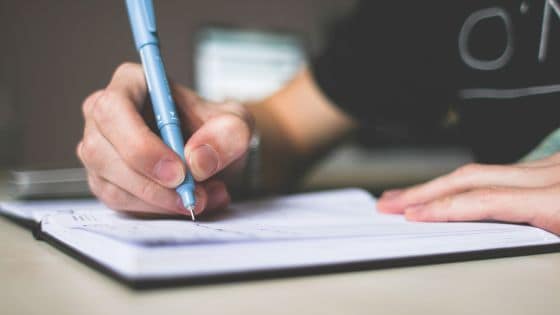 6 consejos de escritura que no funcionan en español 2 Se ve de cerca una mano con un pilot azul escribiendo en un cuaderno.
